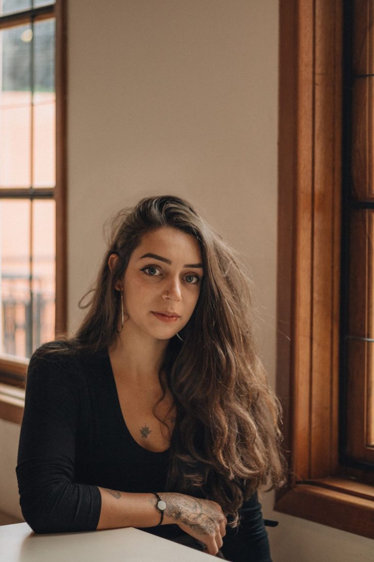 A woman seated beside a wooden window in soft daylight.
