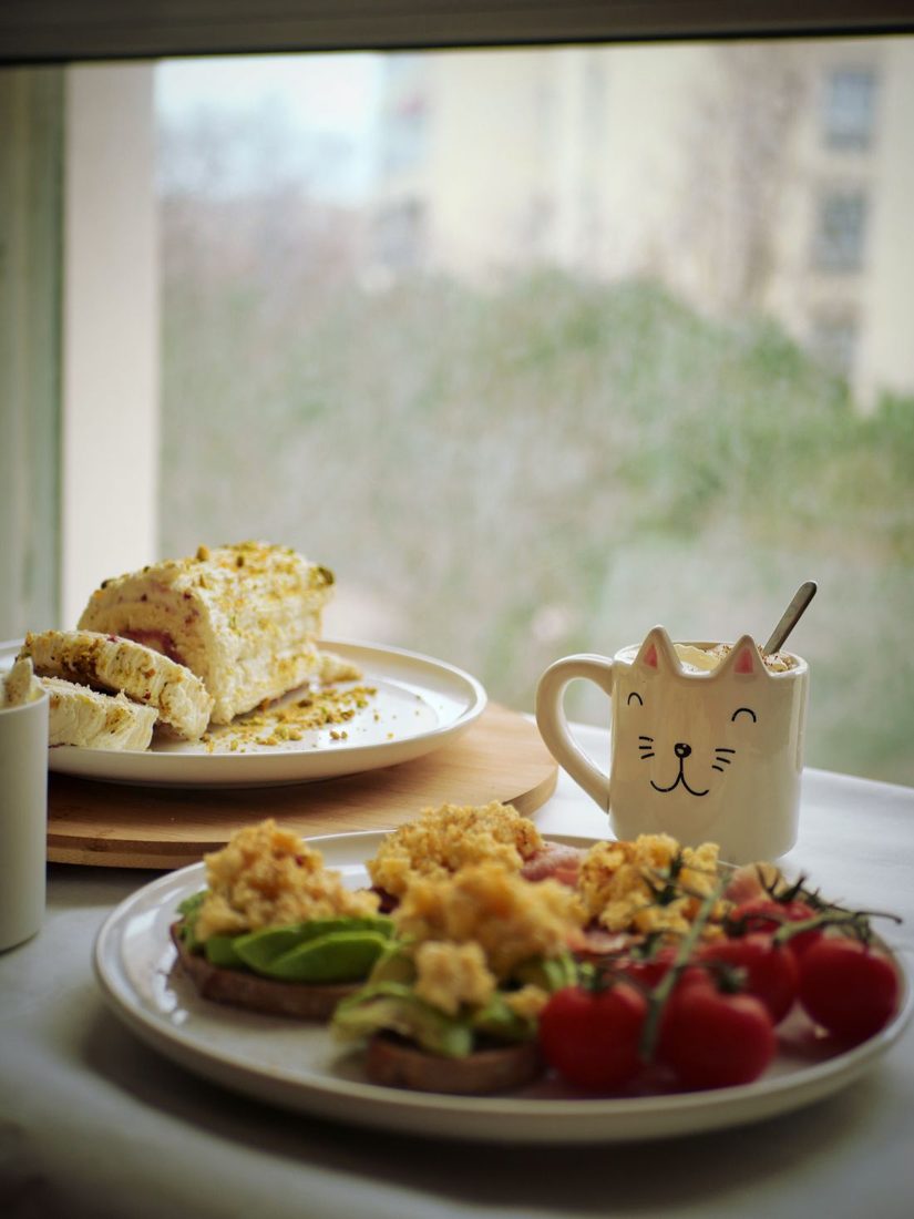 Plates of food and a mug on a table beside a window.