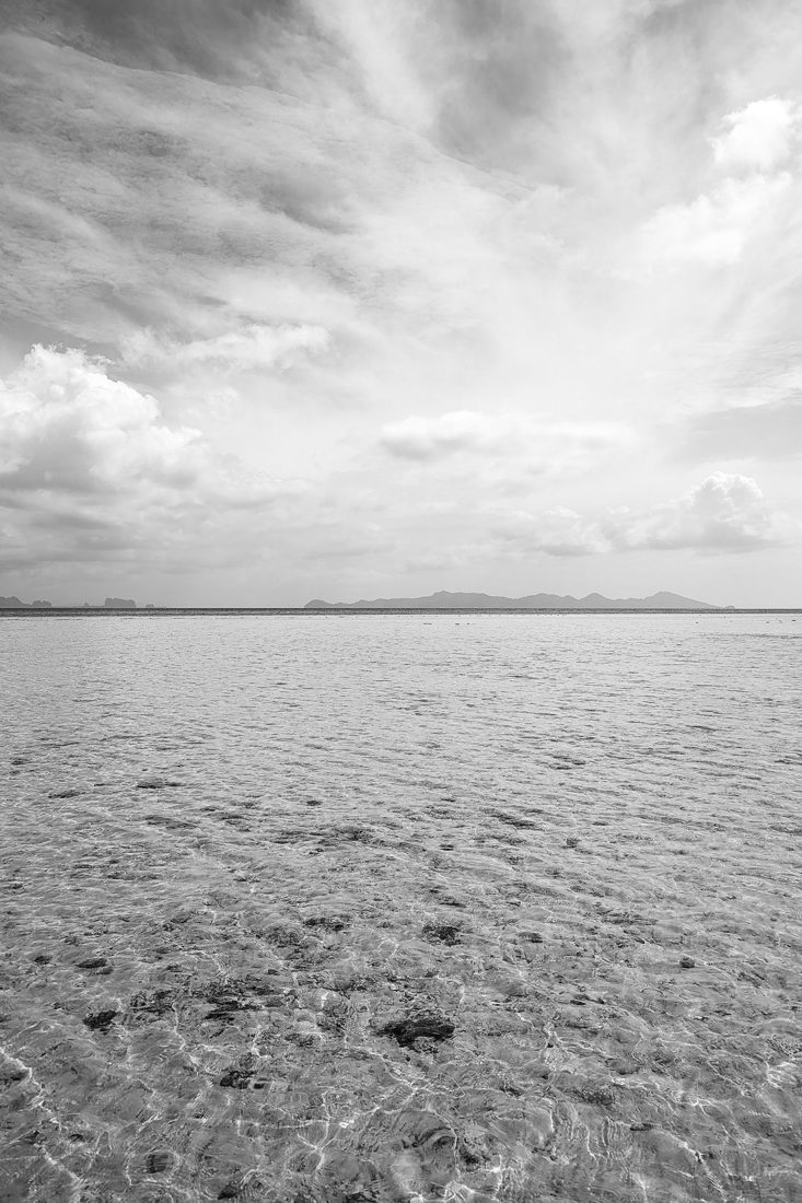 A level sea horizon beneath a cloudy sky in black and white.