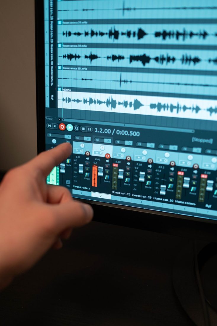 A hand pointing at multitrack audio editing software.