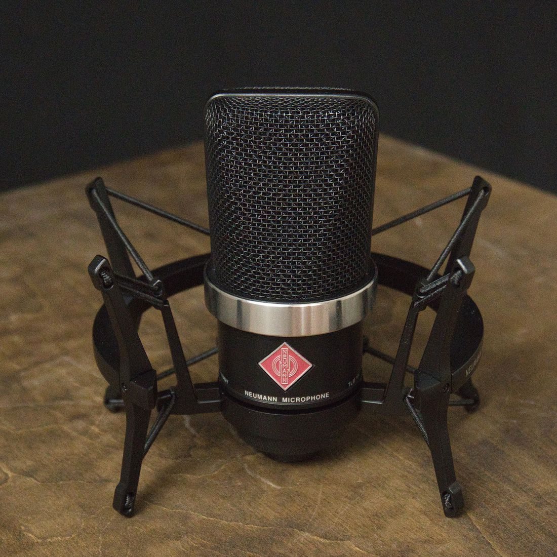 A microphone held in a shock mount on a wooden surface.