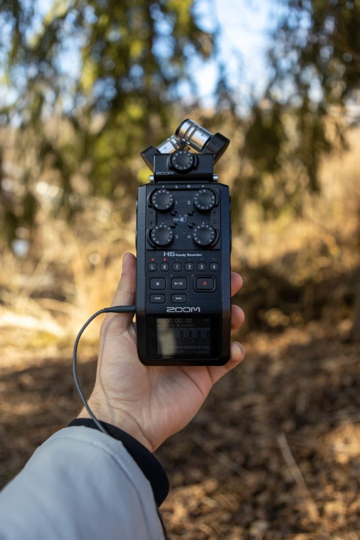 A hand holding a portable audio recorder outdoors.