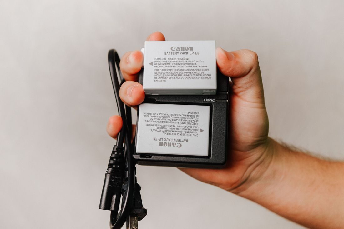A hand holding a camera battery charger and cable.