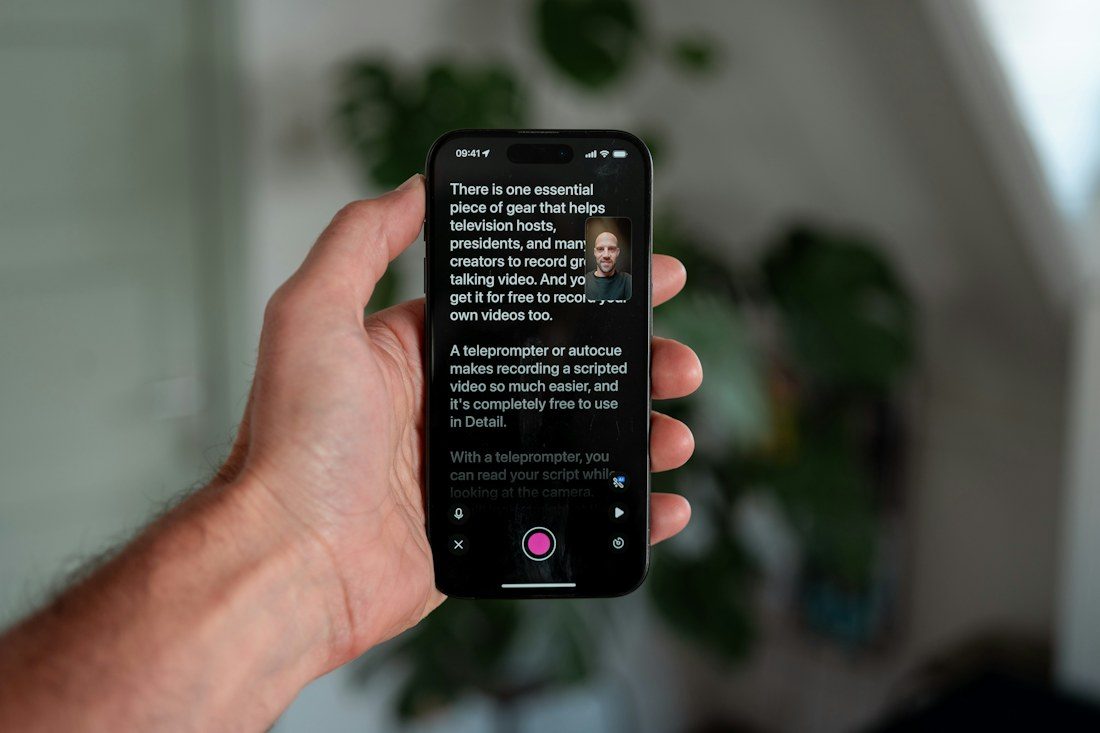 A hand holding a phone with a teleprompter script and presenter preview.