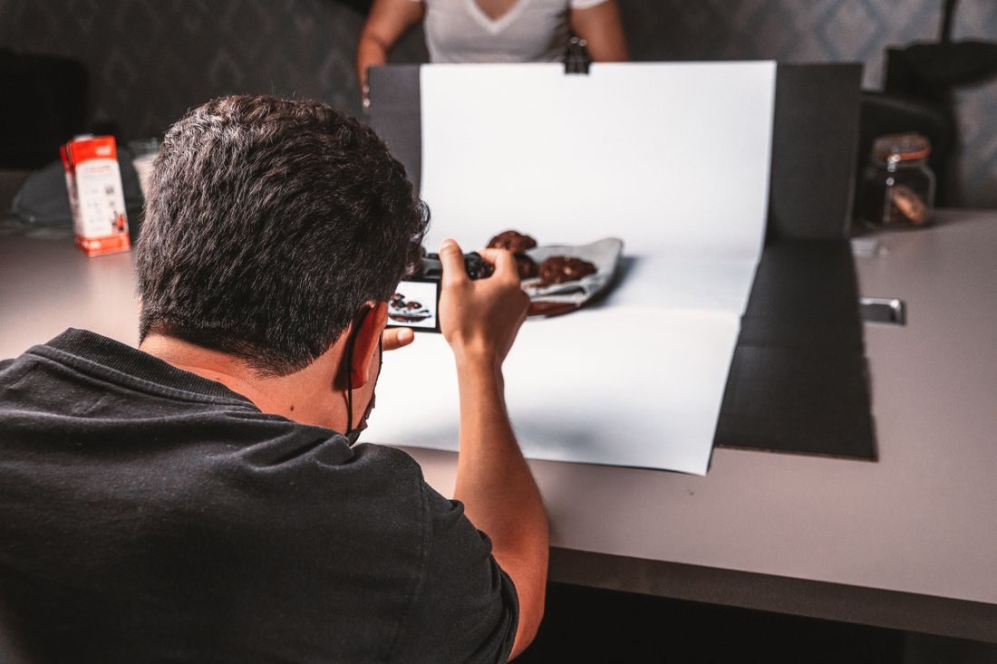 A photographer working at a small tabletop setup with a white backdrop.