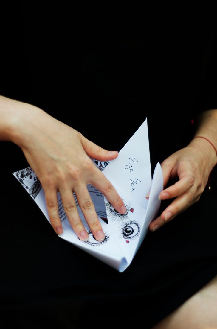 Hands folding a decorated piece of paper.
