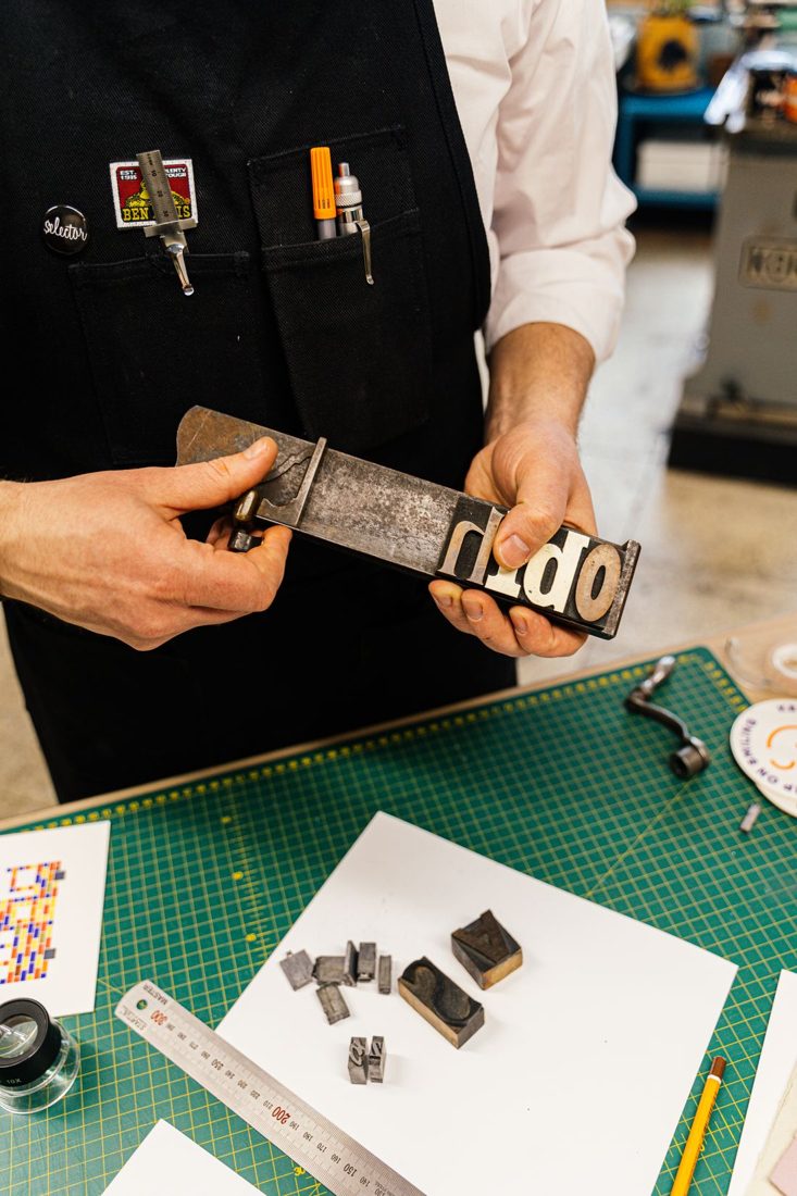 Hands arranging a typography printing block in a workshop.